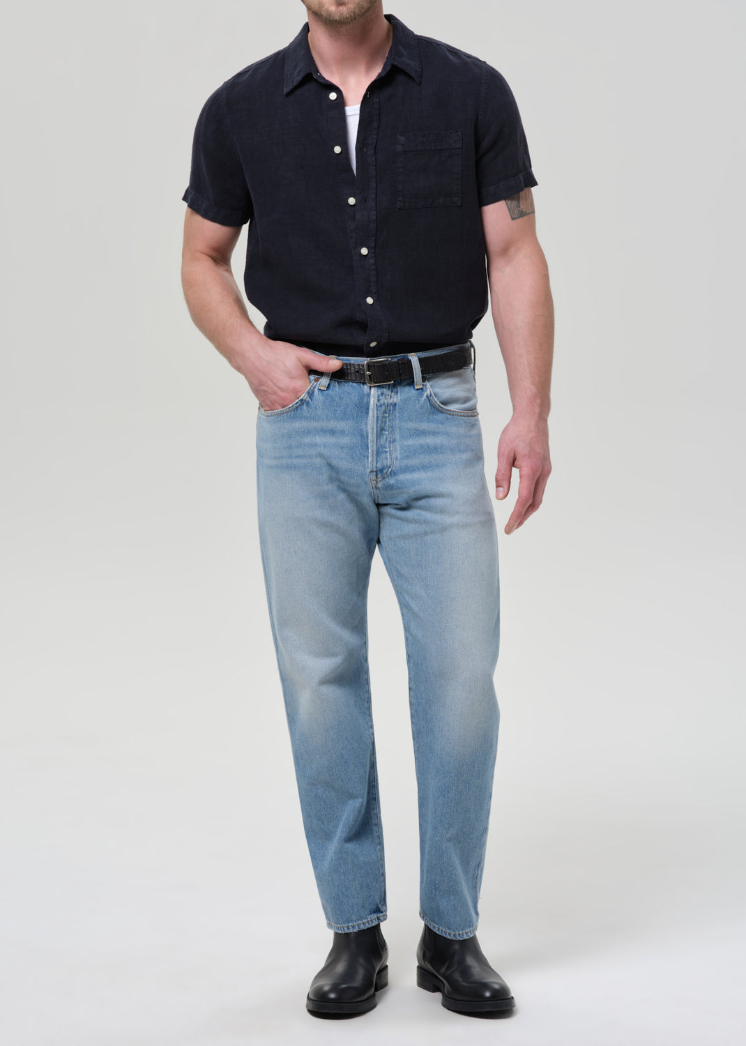 Man wearing a navy button-up shirt and light blue jeans on a plain background