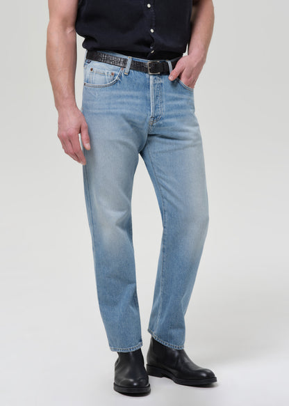 Man wearing a navy button-up shirt and light blue jeans on a plain background