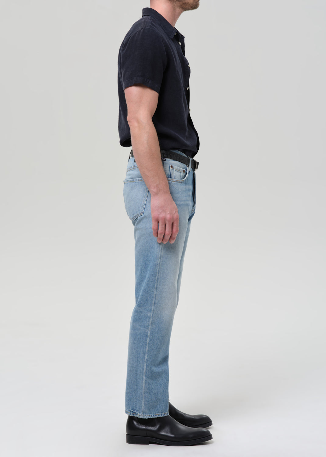 Man wearing a navy button-up shirt and light blue jeans on a plain background