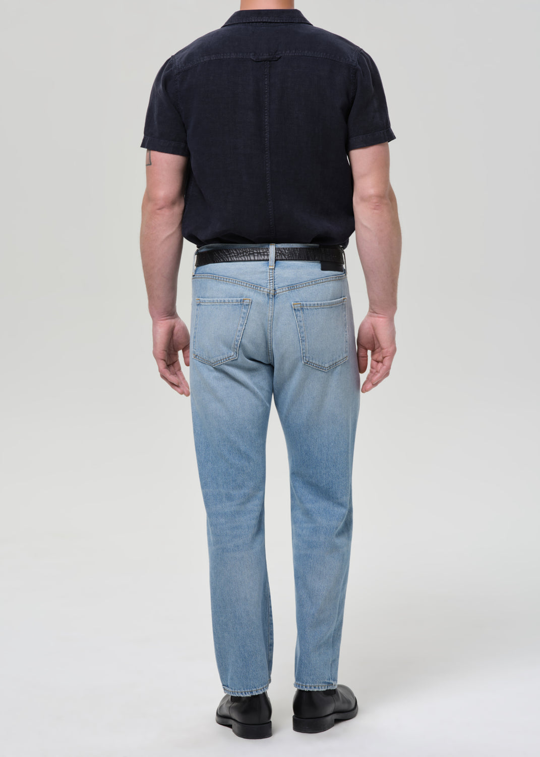 Man wearing a navy button-up shirt and light blue jeans on a plain background