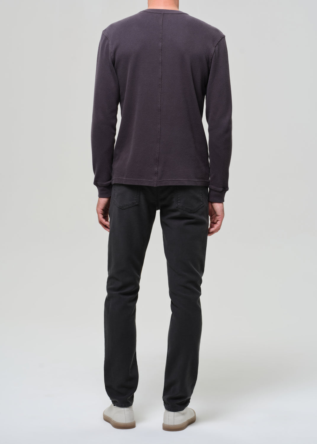 Person wearing a dark crewneck and dark grey pants on a plain background