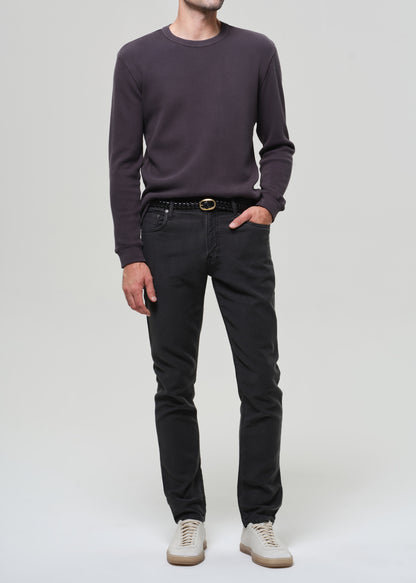 Person wearing a dark crewneck and dark grey pants on a plain background