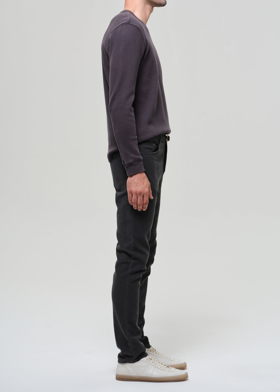 Person wearing a dark crewneck and dark grey pants on a plain background
