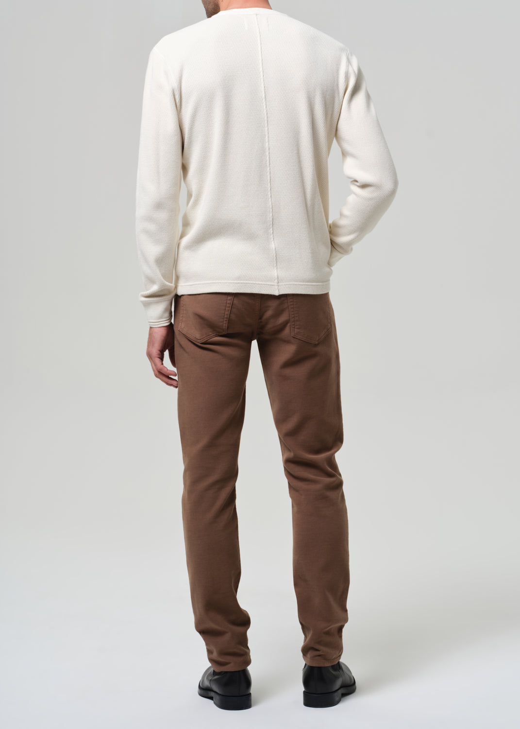 Man wearing a white henley and brown pants on a plain background