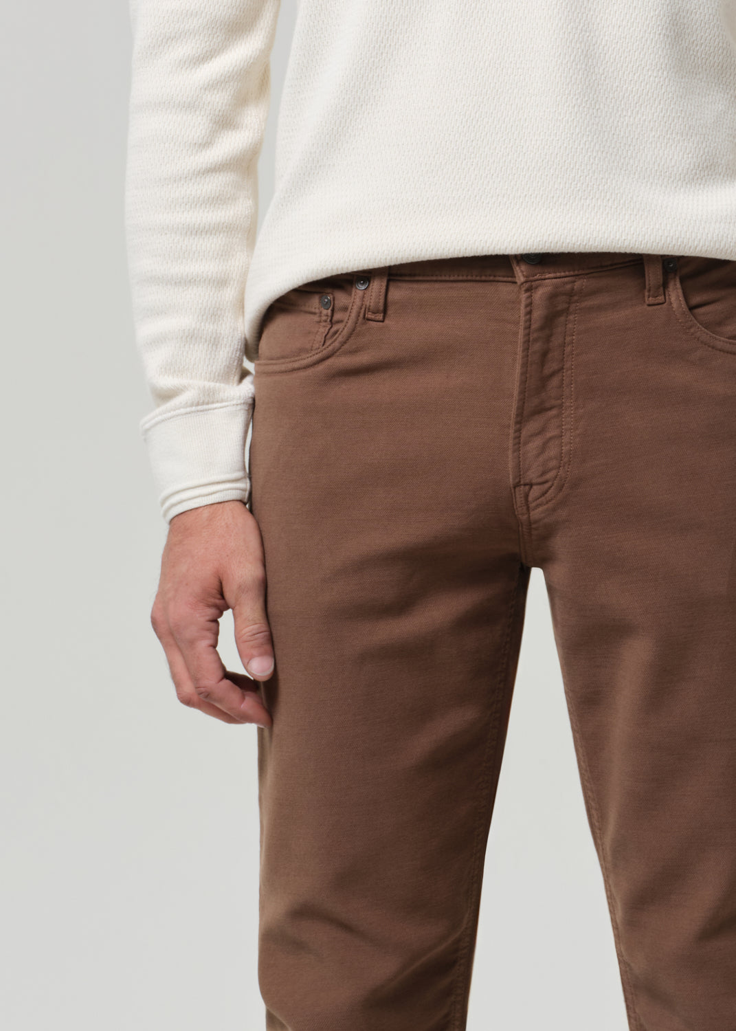 Man wearing a white henley and brown pants on a plain background