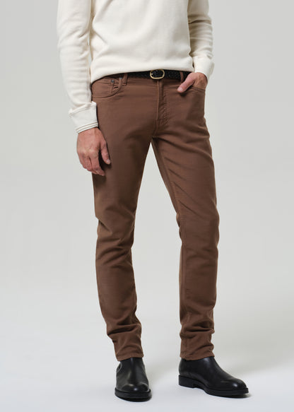 Man wearing a white henley and brown pants on a plain background