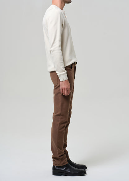 Man wearing a white henley and brown pants on a plain background