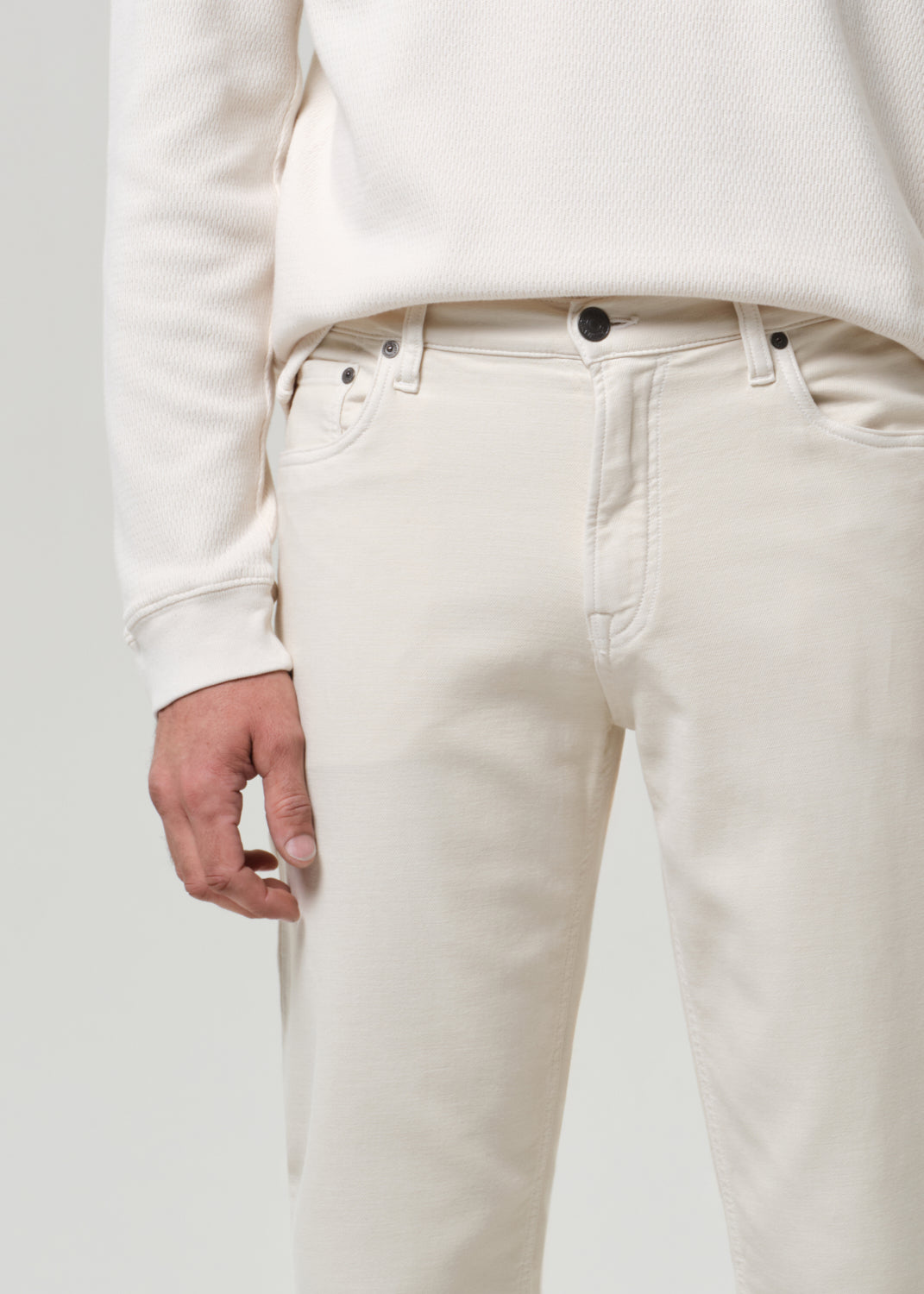 Person wearing a white crewneck and cream pants with black shoes on a plain background