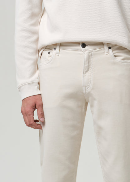 Person wearing a white crewneck and cream pants with black shoes on a plain background