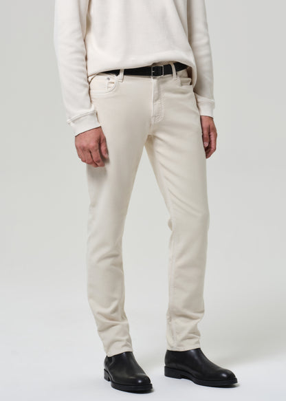 Person wearing a white crewneck and cream pants with black shoes on a plain background