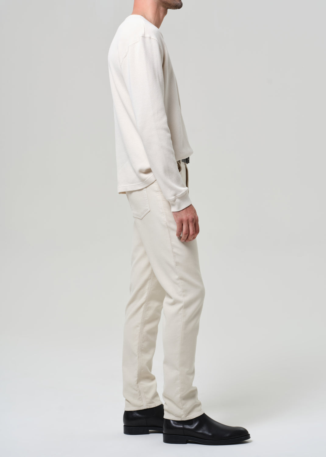 Person wearing a white crewneck and cream pants with black shoes on a plain background