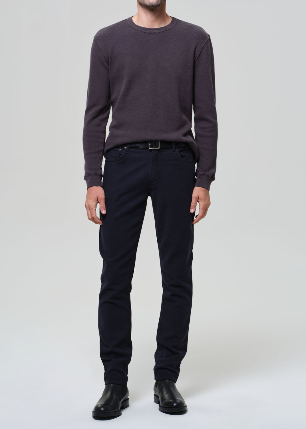 Person wearing a dark grey crewneck and navy pants on a grey background