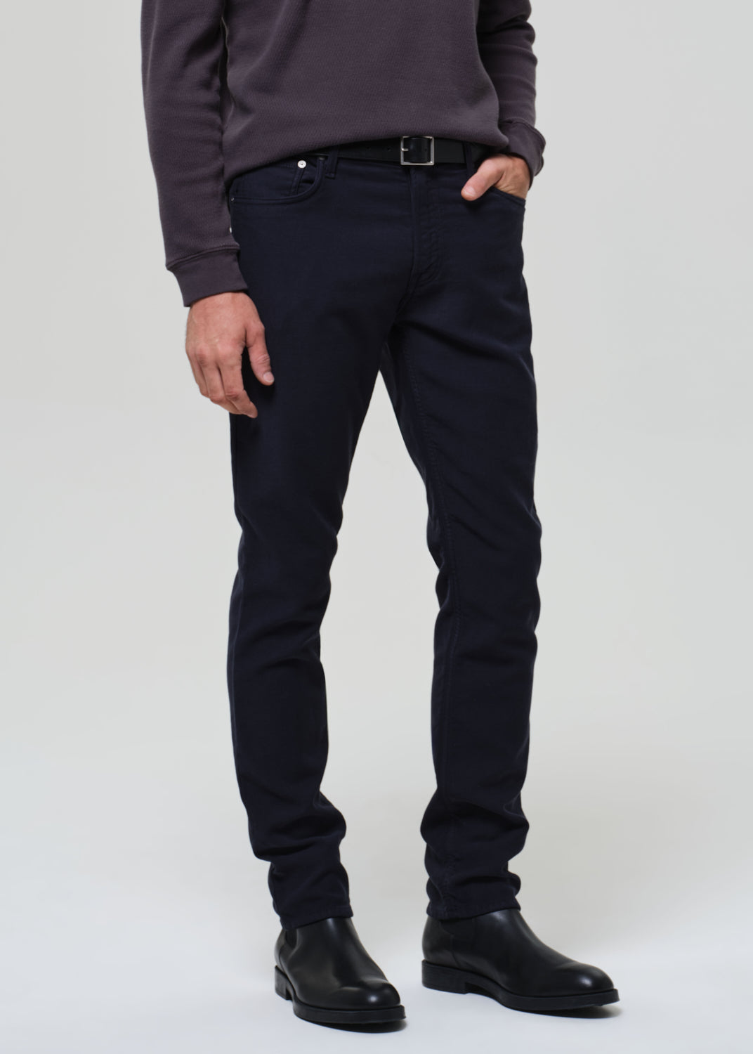 Person wearing a dark grey crewneck and navy pants on a grey background