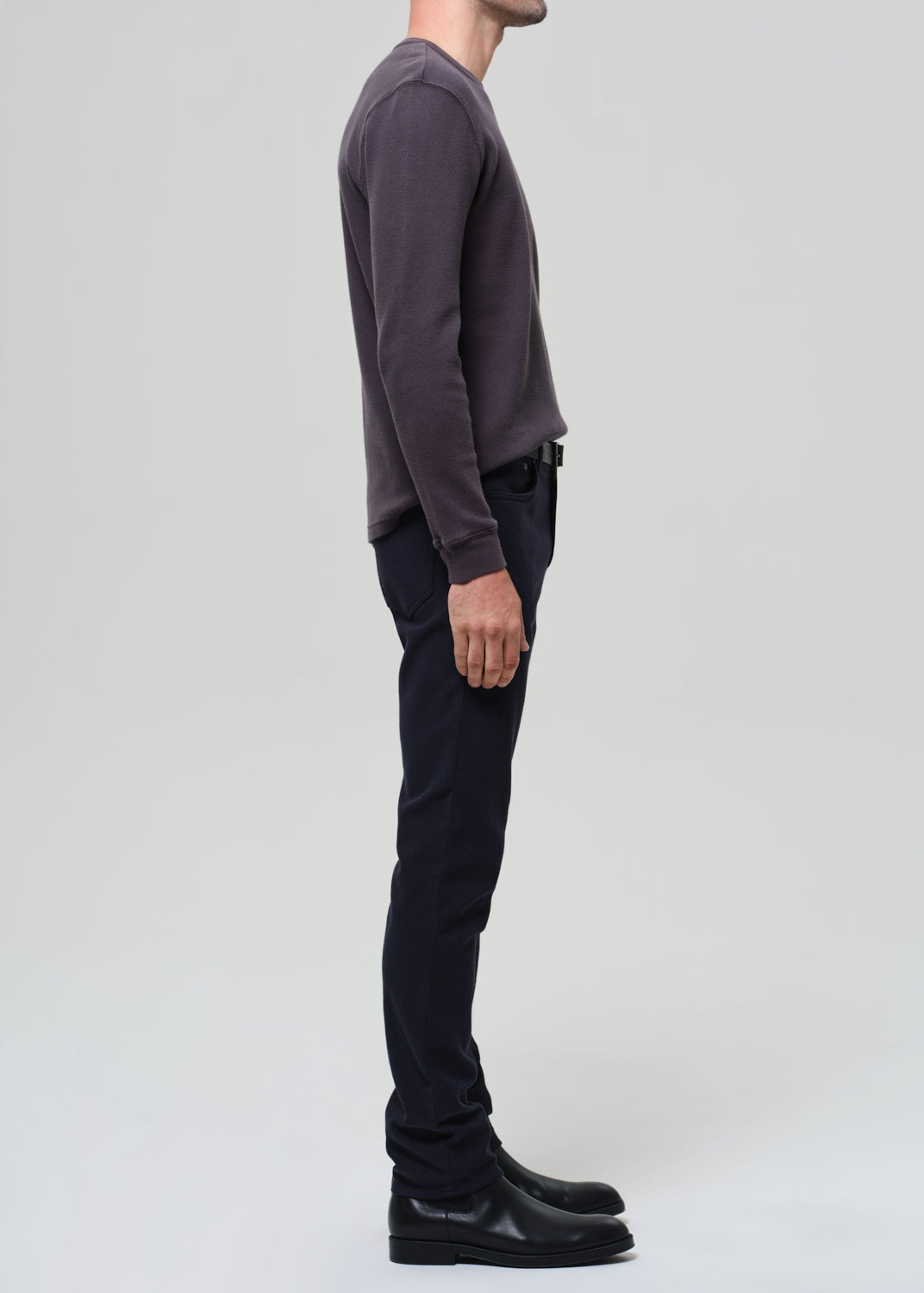 Person wearing a dark grey crewneck and navy pants on a grey background