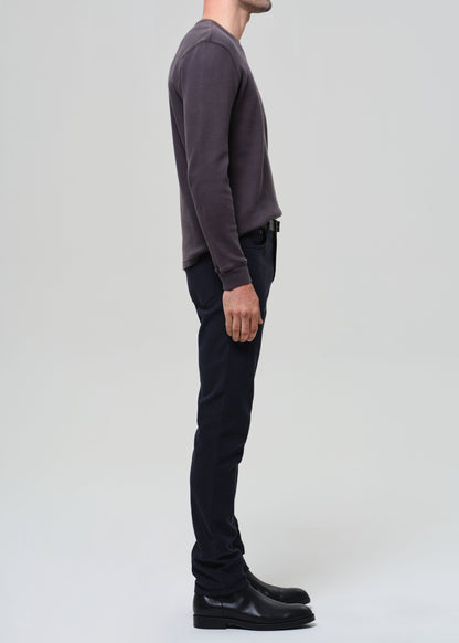 Person wearing a dark grey crewneck and navy pants on a grey background
