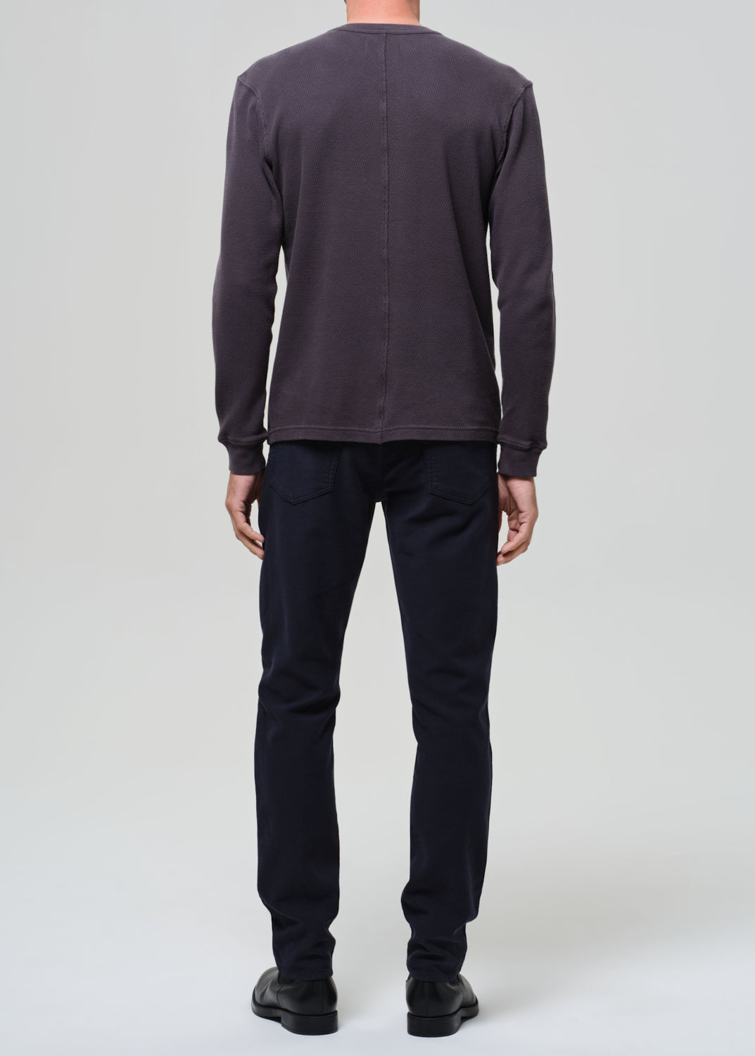 Person wearing a dark grey crewneck and navy pants on a grey background