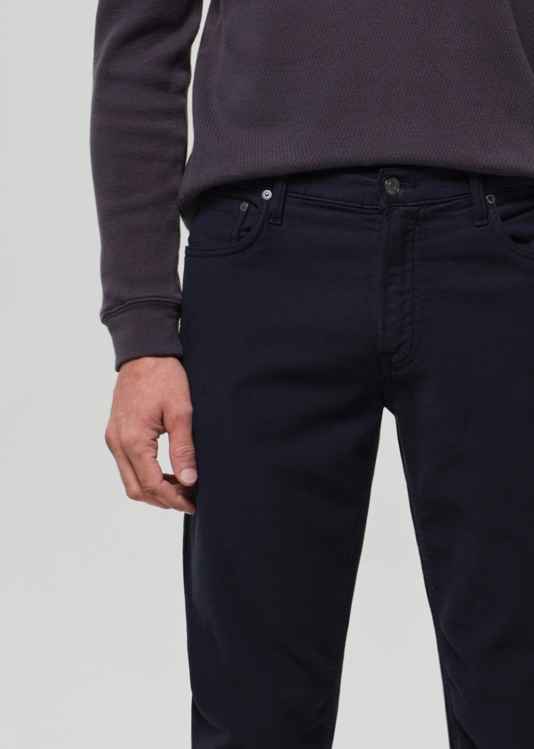 Person wearing a dark grey crewneck and navy pants on a grey background