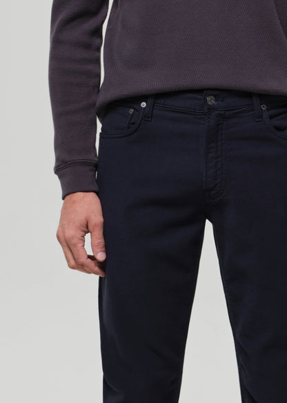Person wearing a dark grey crewneck and navy pants on a grey background