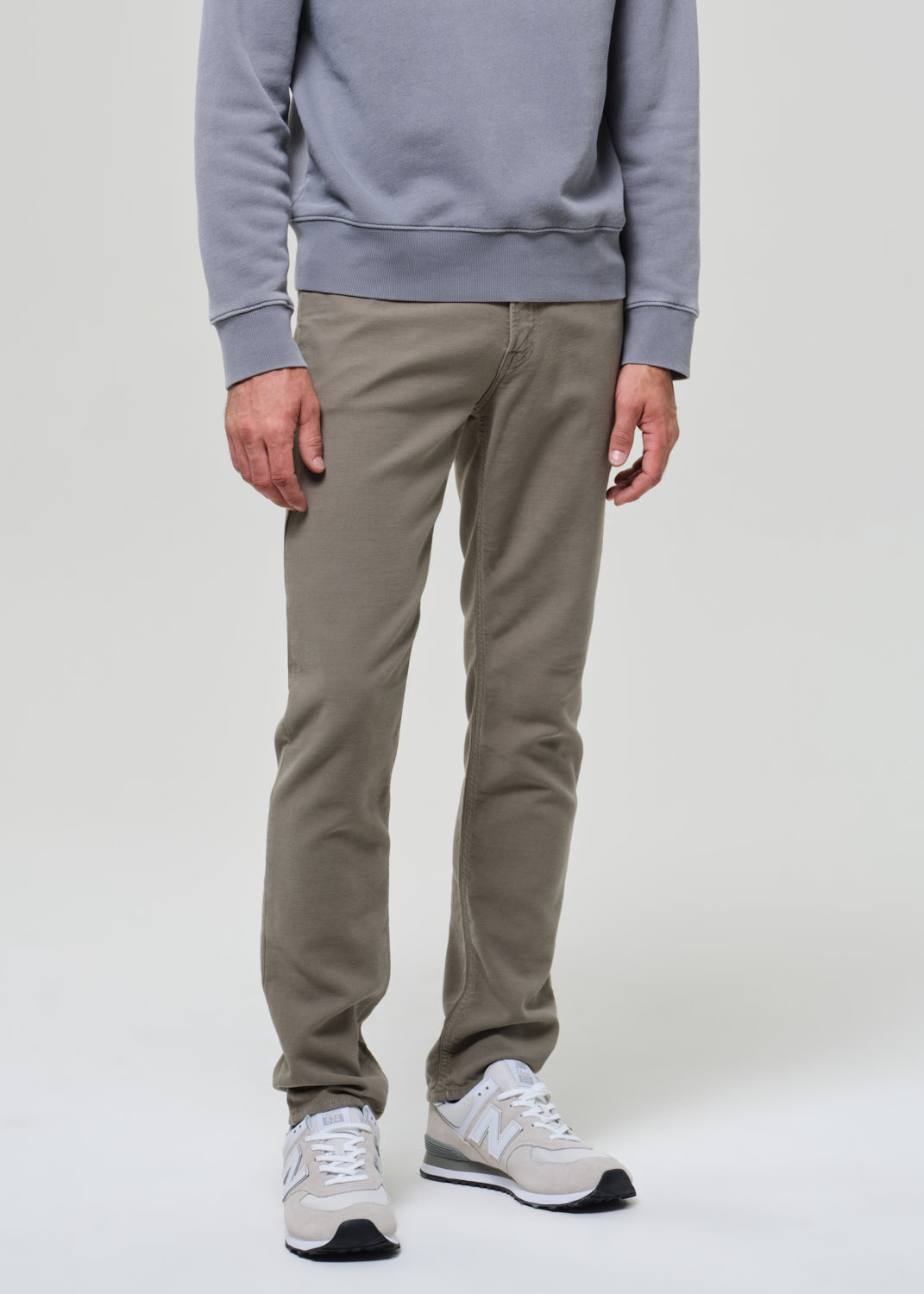 Person wearing a gray sweatshirt and green pants on a grey background