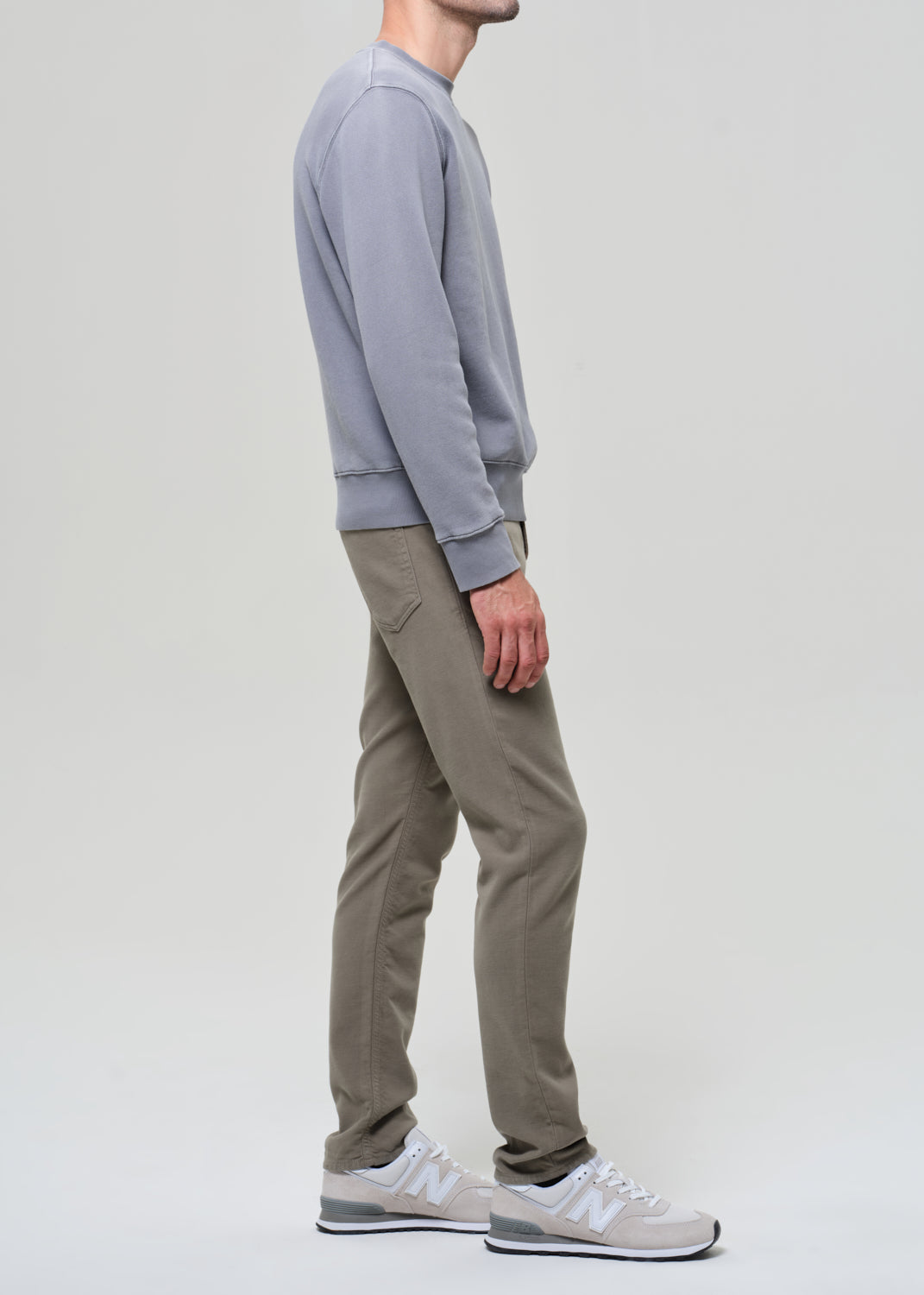 Person wearing a gray sweatshirt and green pants on a grey background