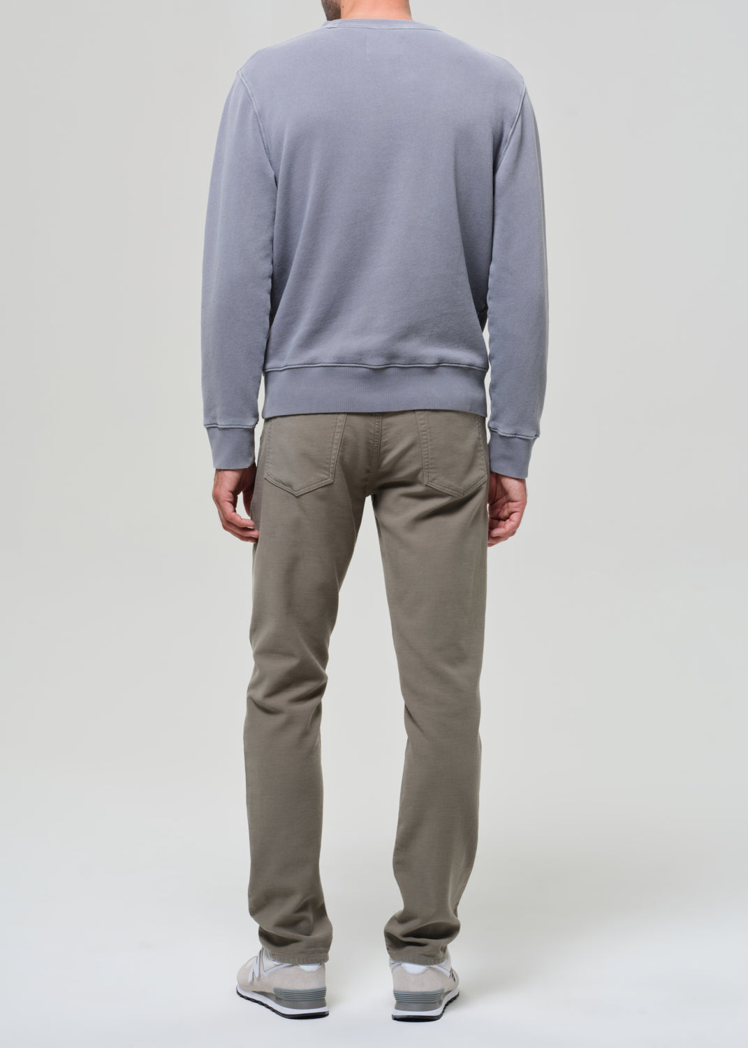 Person wearing a gray sweatshirt and green pants on a grey background