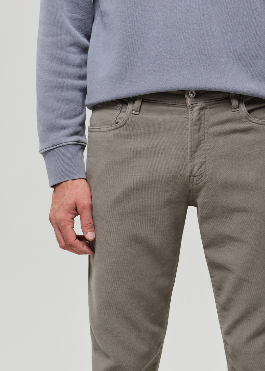 Person wearing a gray sweatshirt and green pants on a grey background