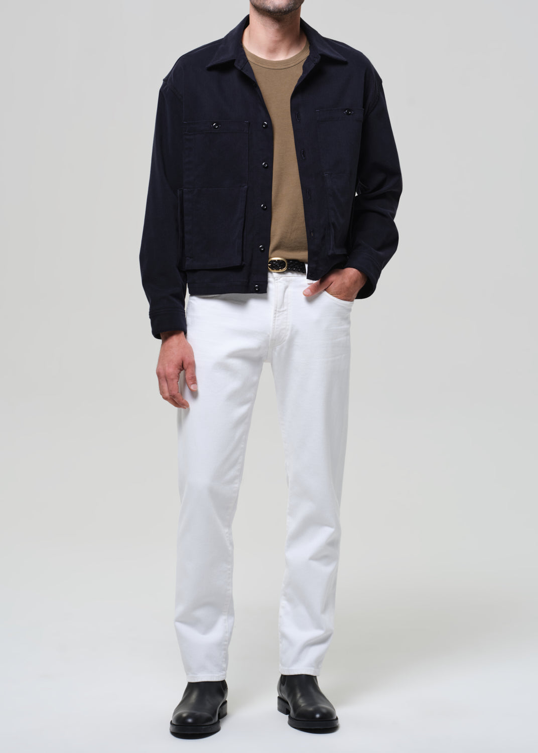 Person wearing a navy jacket, beige shirt, white pants, and black shoes on a light gray background