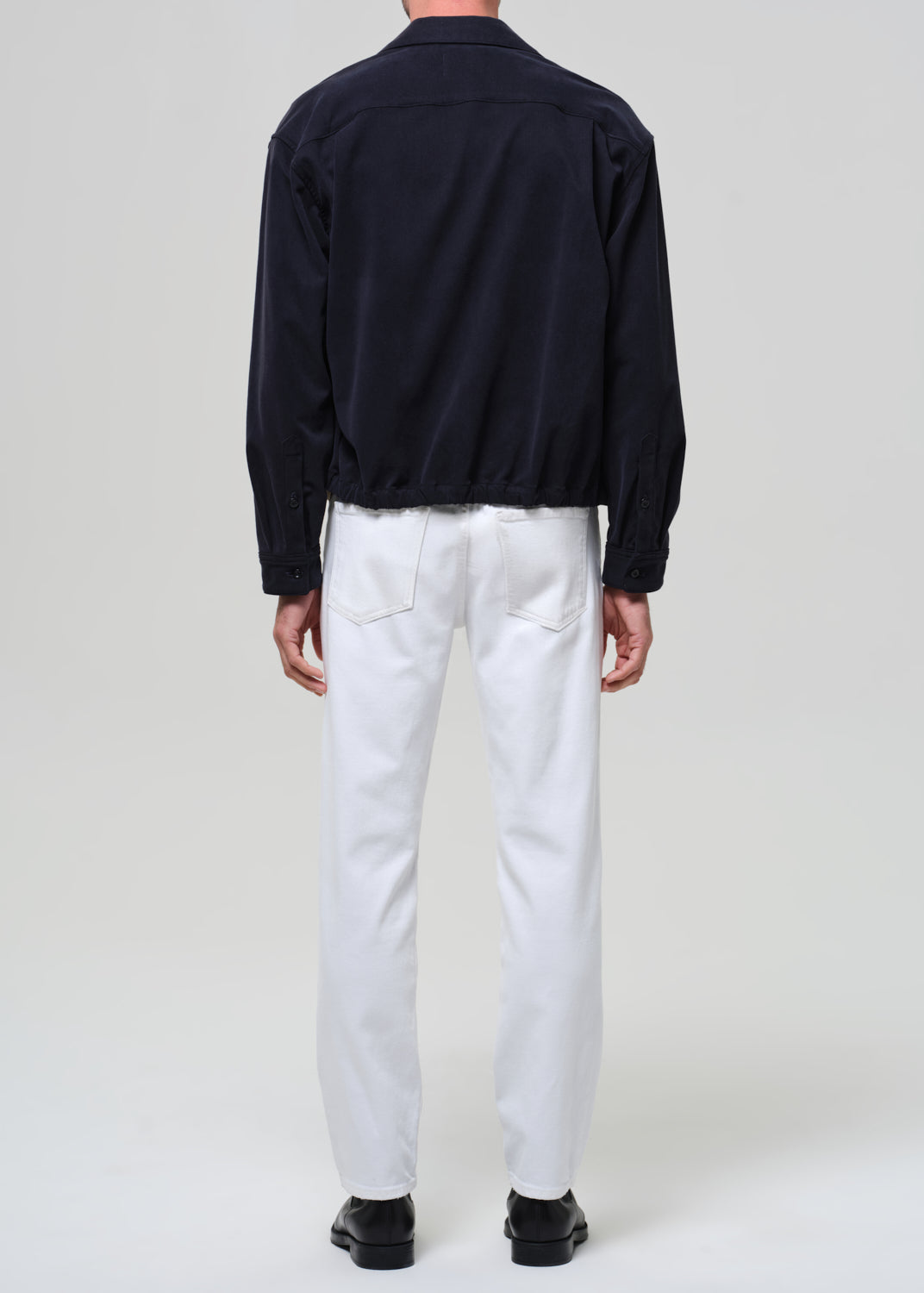 Person wearing a dark jacket and white pants on a plain background