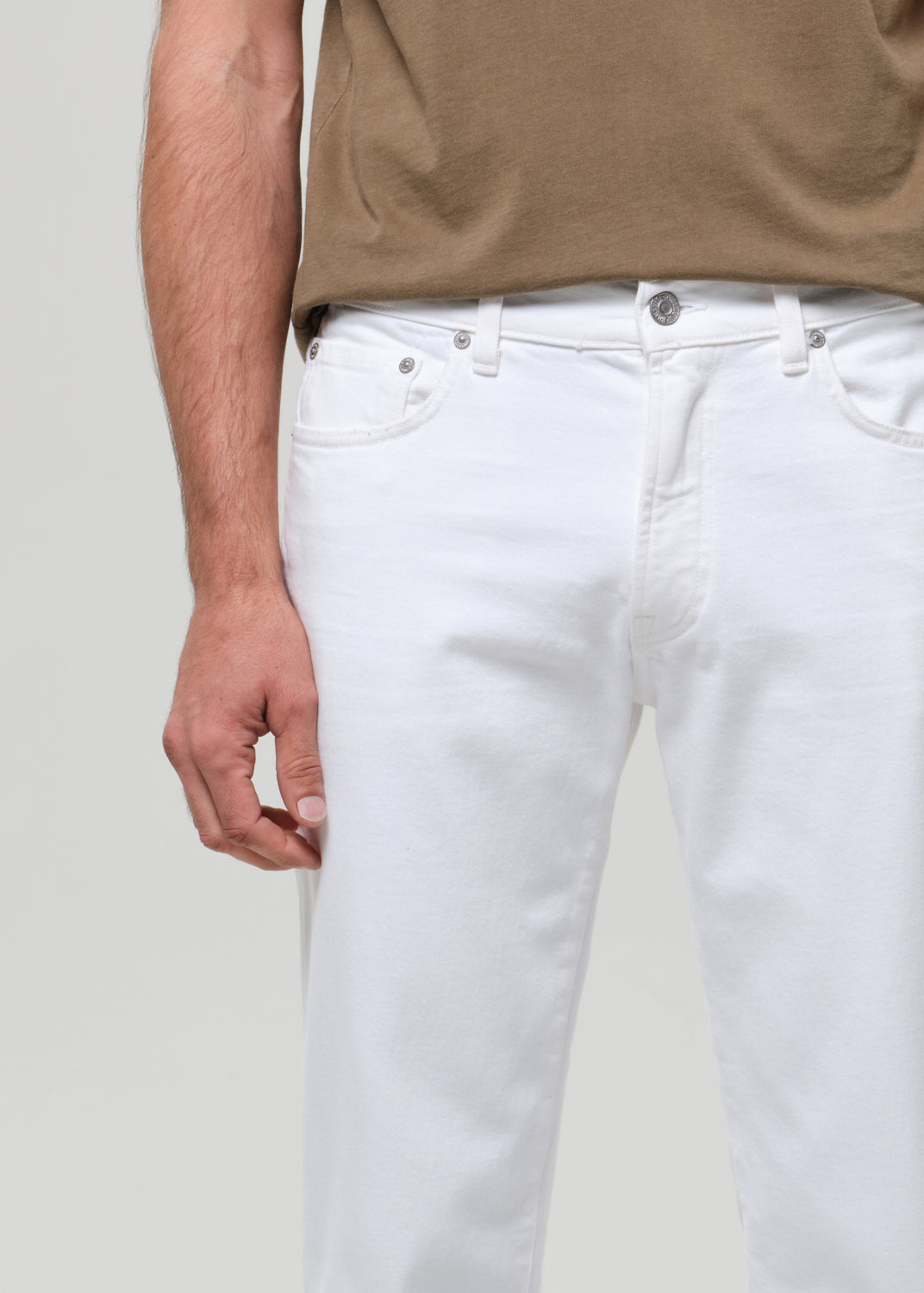 Person wearing white jeans and a brown shirt on a plain background