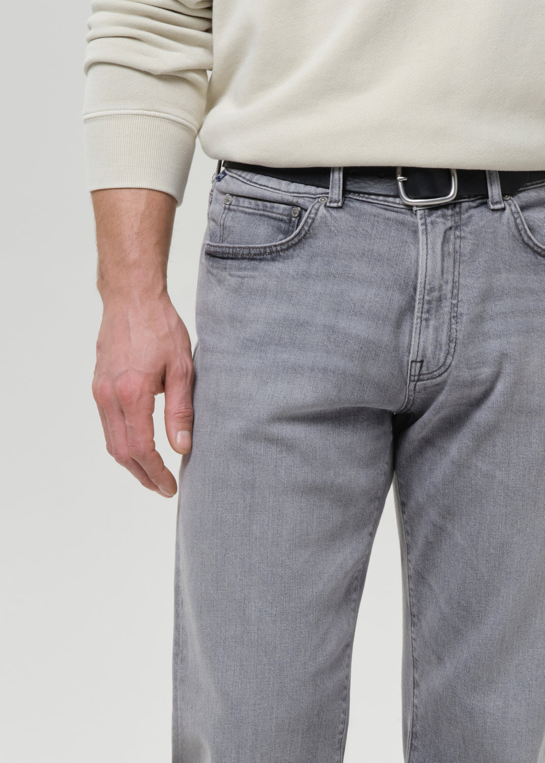 Person wearing light grey jeans and a beige sweater on a grey background