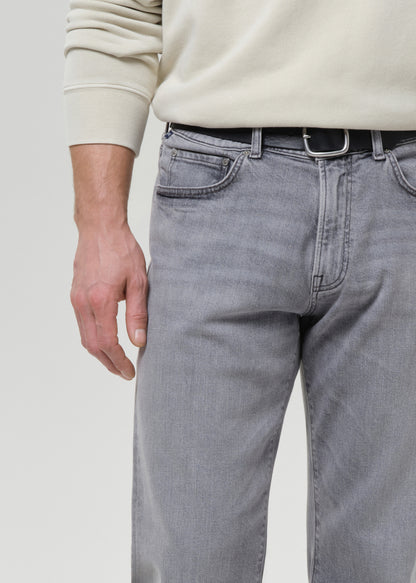 Person wearing light grey jeans and a beige sweater on a grey background