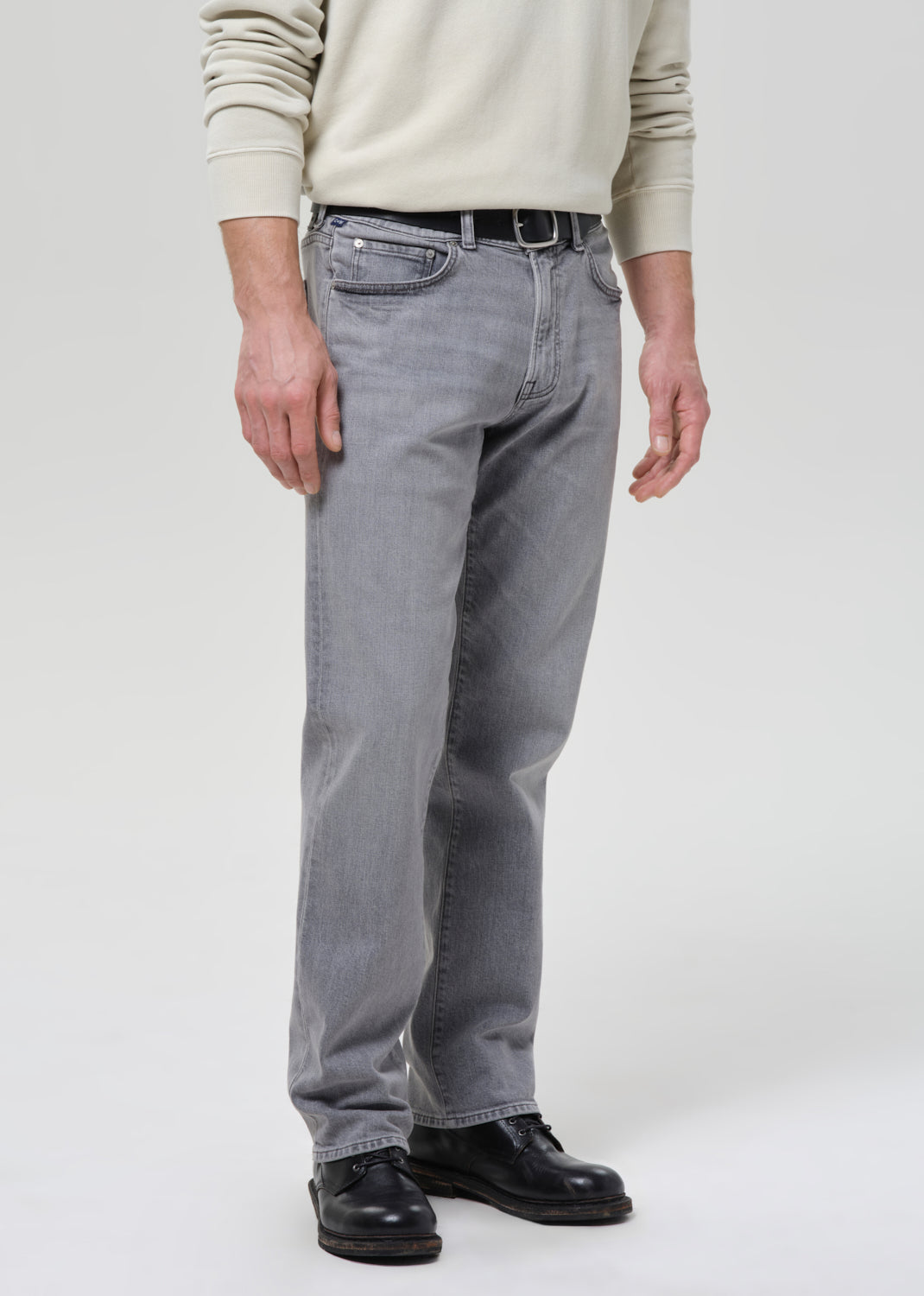 Person wearing grey jeans and a beige sweater on a grey background