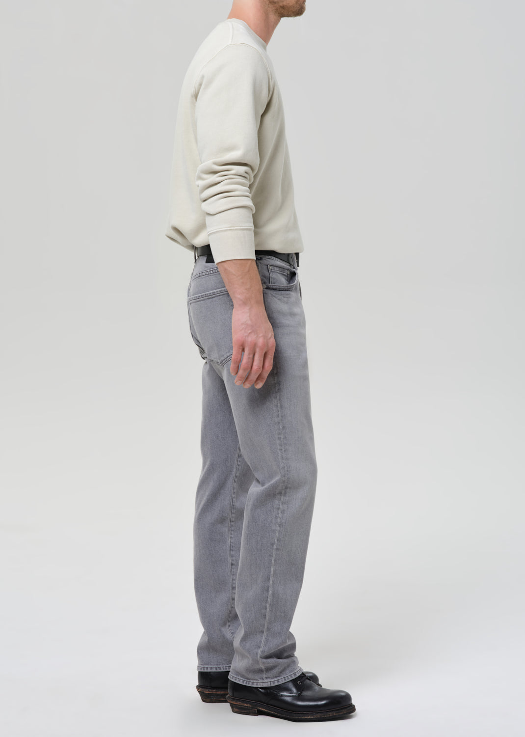 Person wearing a light-colored sweater and grey jeans on a grey background