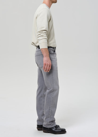 Person wearing a light-colored sweater and grey jeans on a grey background