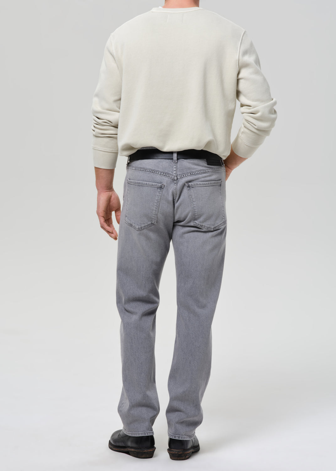 Person wearing a light-colored sweater and grey jeans on a grey background