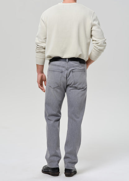 Person wearing a light-colored sweater and grey jeans on a grey background