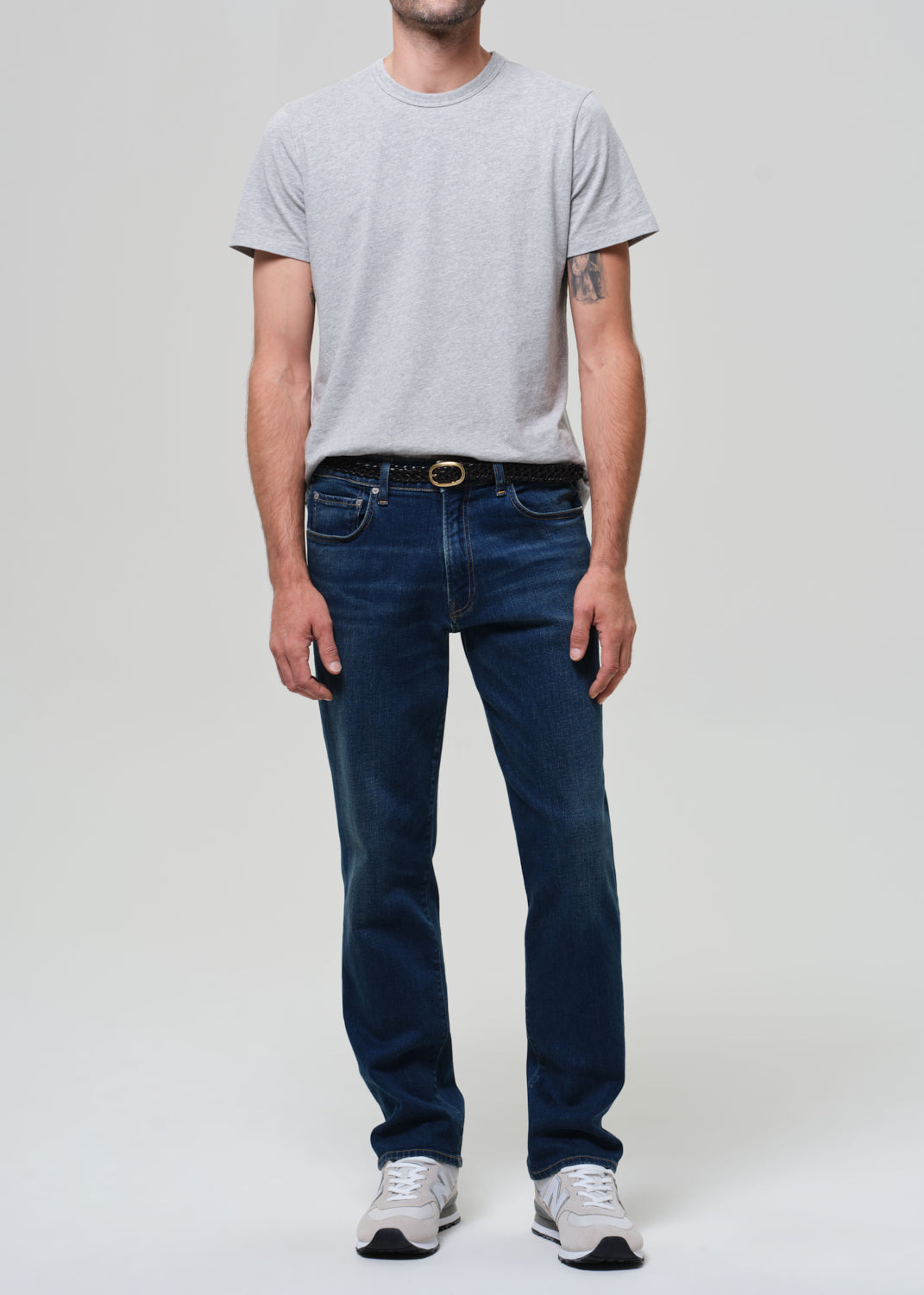Person wearing a gray t-shirt and dark blue jeans on a plain background
