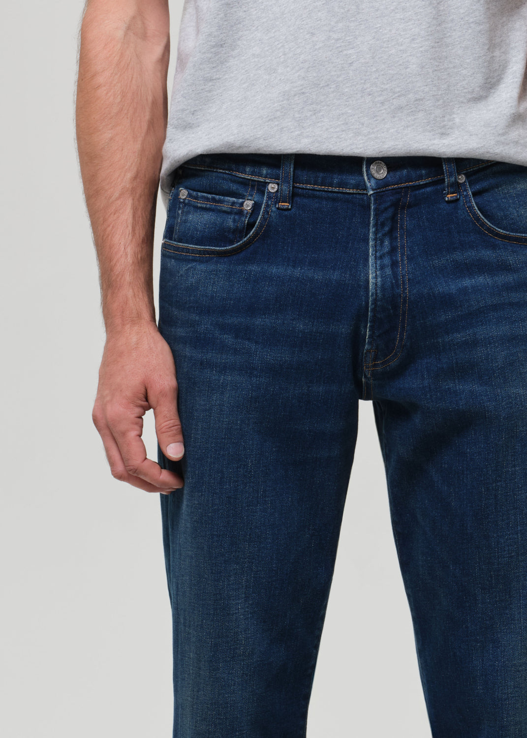 Person wearing blue jeans and a gray shirt on a plain background