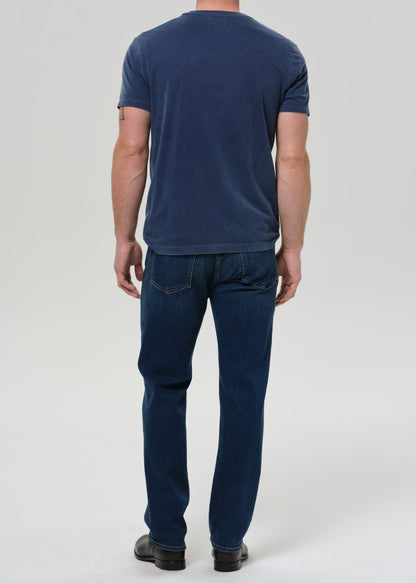 A man viewed from behind wearing a dark blue t-shirt and dark blue jeans, standing against a grey background.