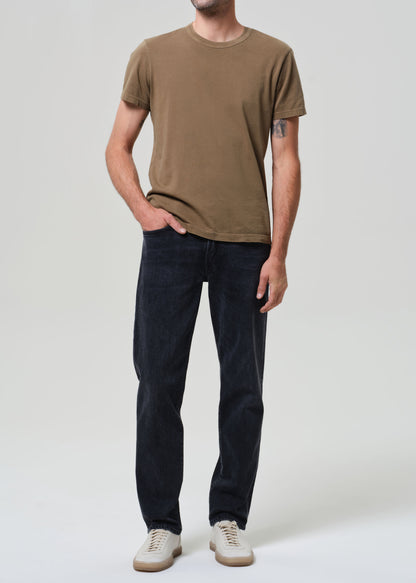 Person wearing a brown t-shirt and dark jeans on a grey background