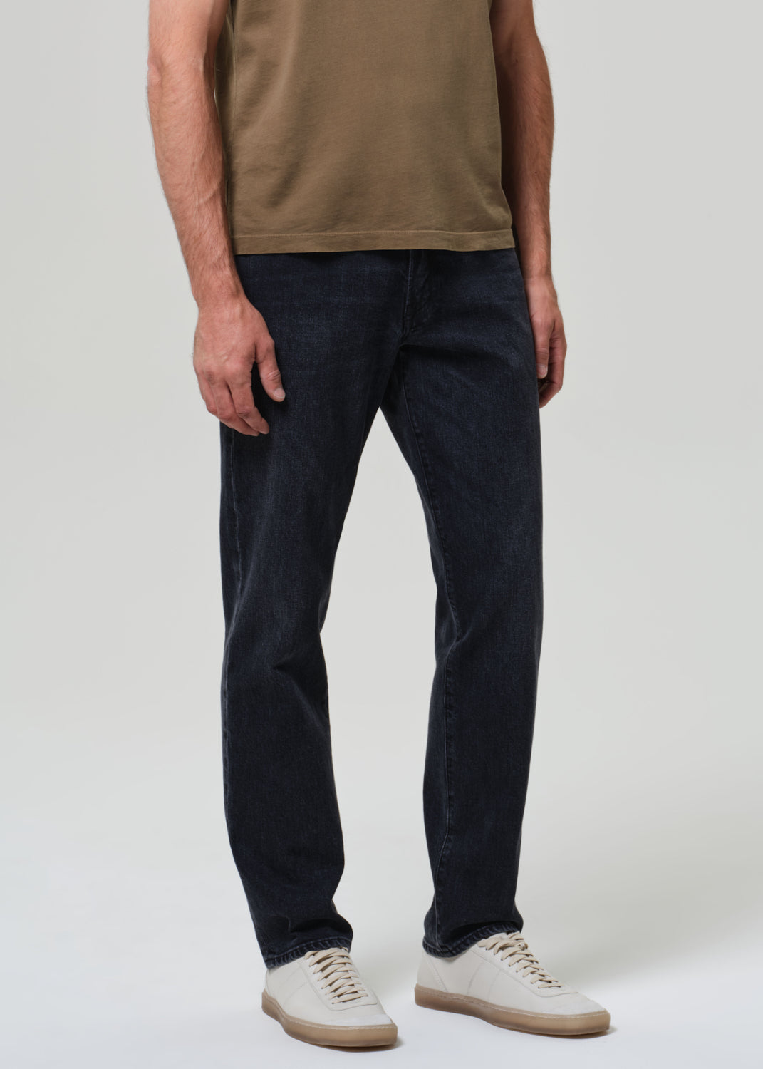Person wearing a brown t-shirt and dark jeans on a grey background