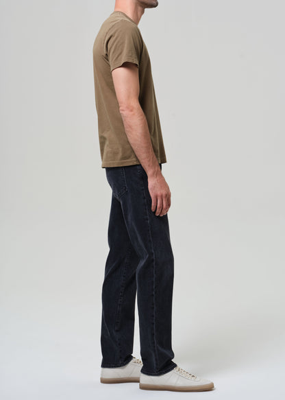 Person wearing a brown t-shirt and dark jeans on a grey background