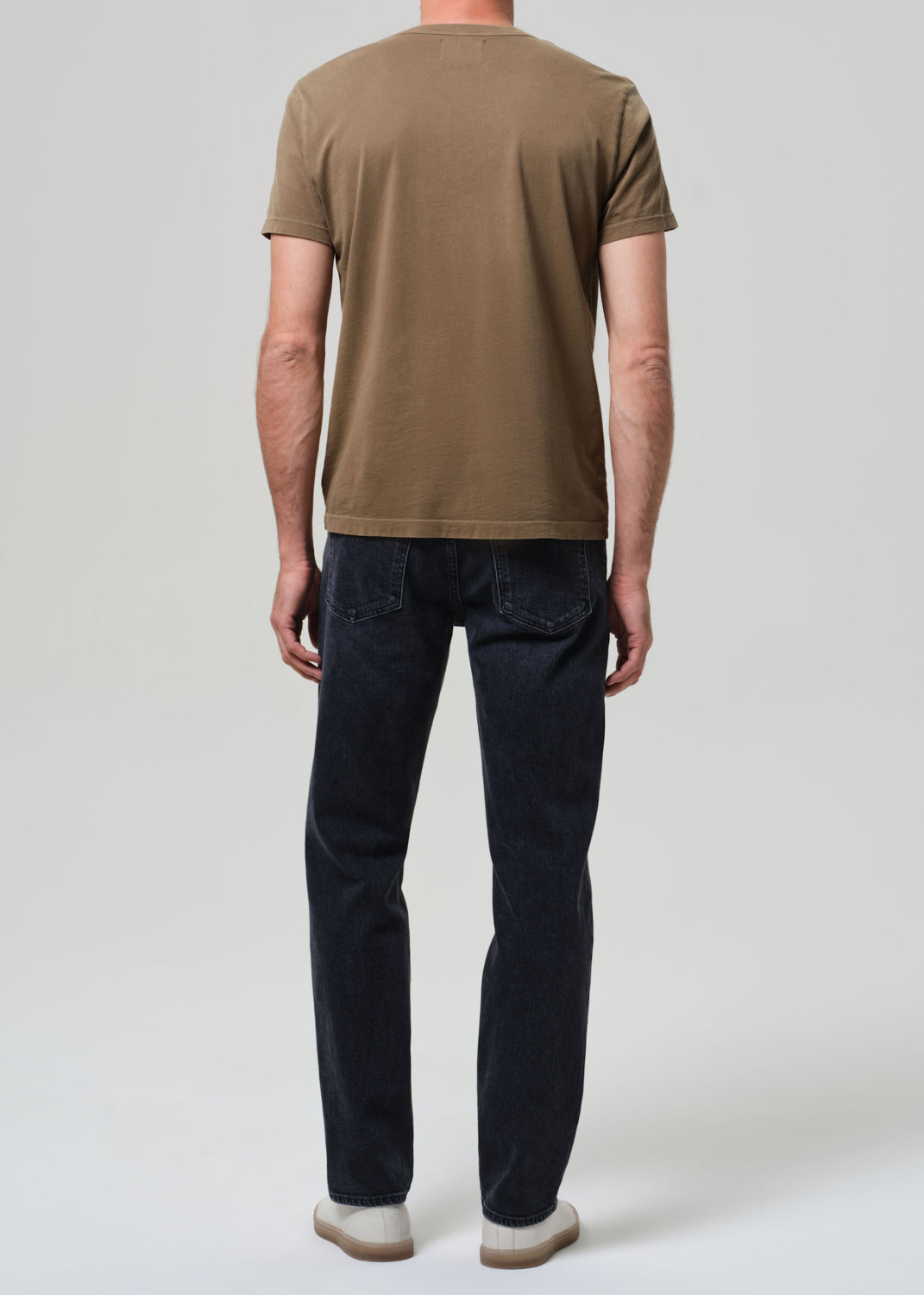 Person wearing a brown t-shirt and dark jeans on a grey background