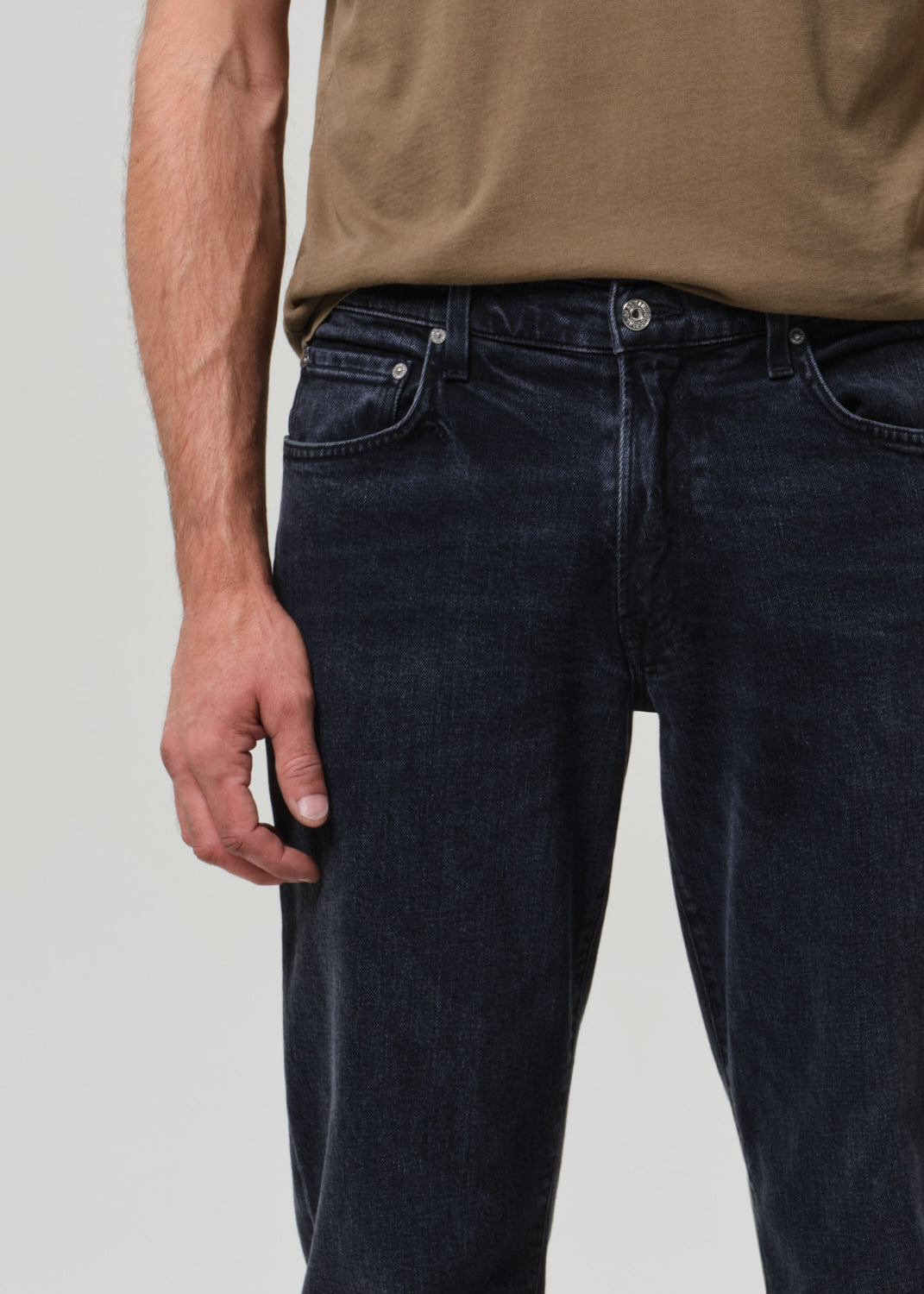 Person wearing a brown t-shirt and dark jeans on a grey background