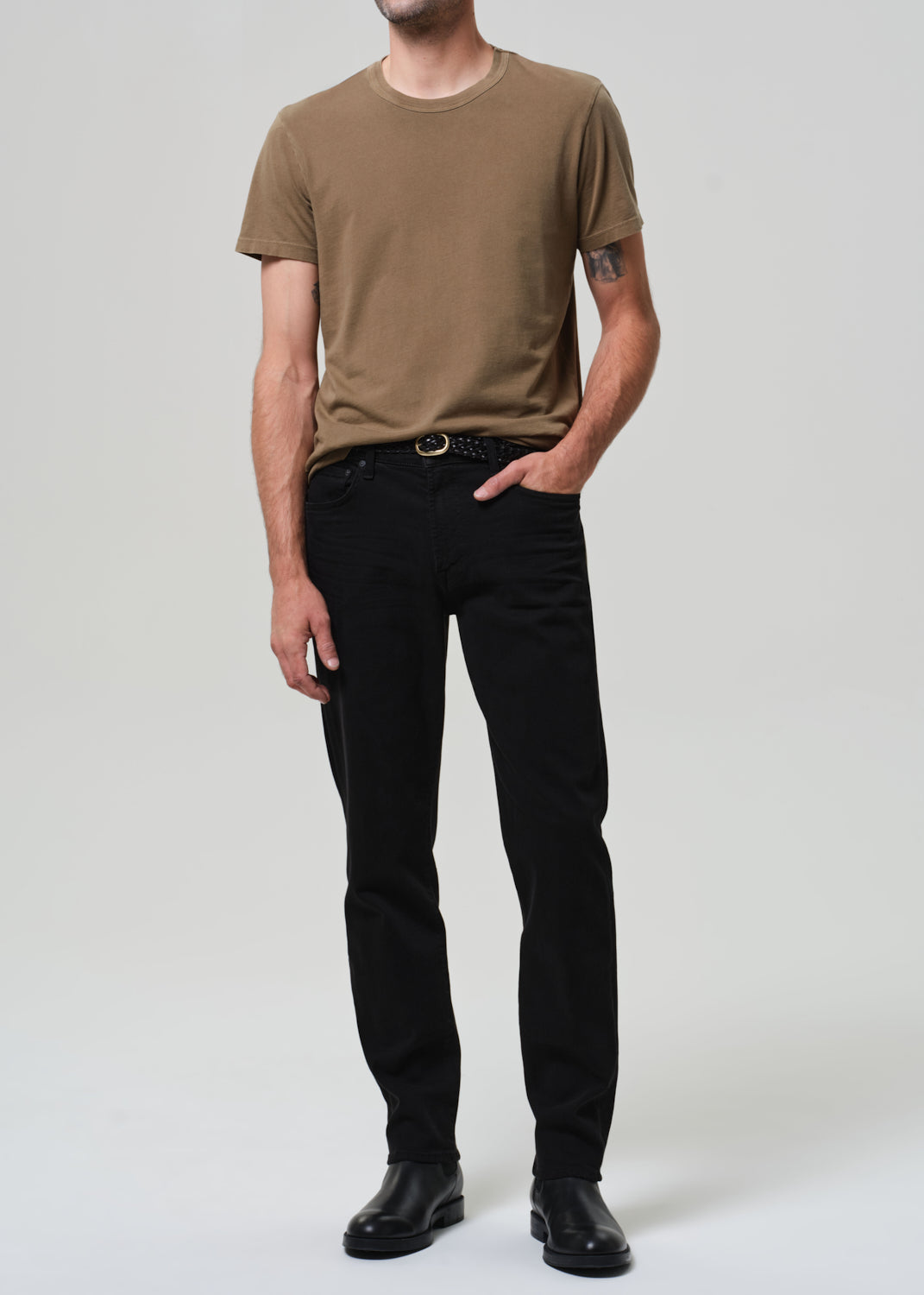 Person wearing a brown t-shirt and black pants on a plain background