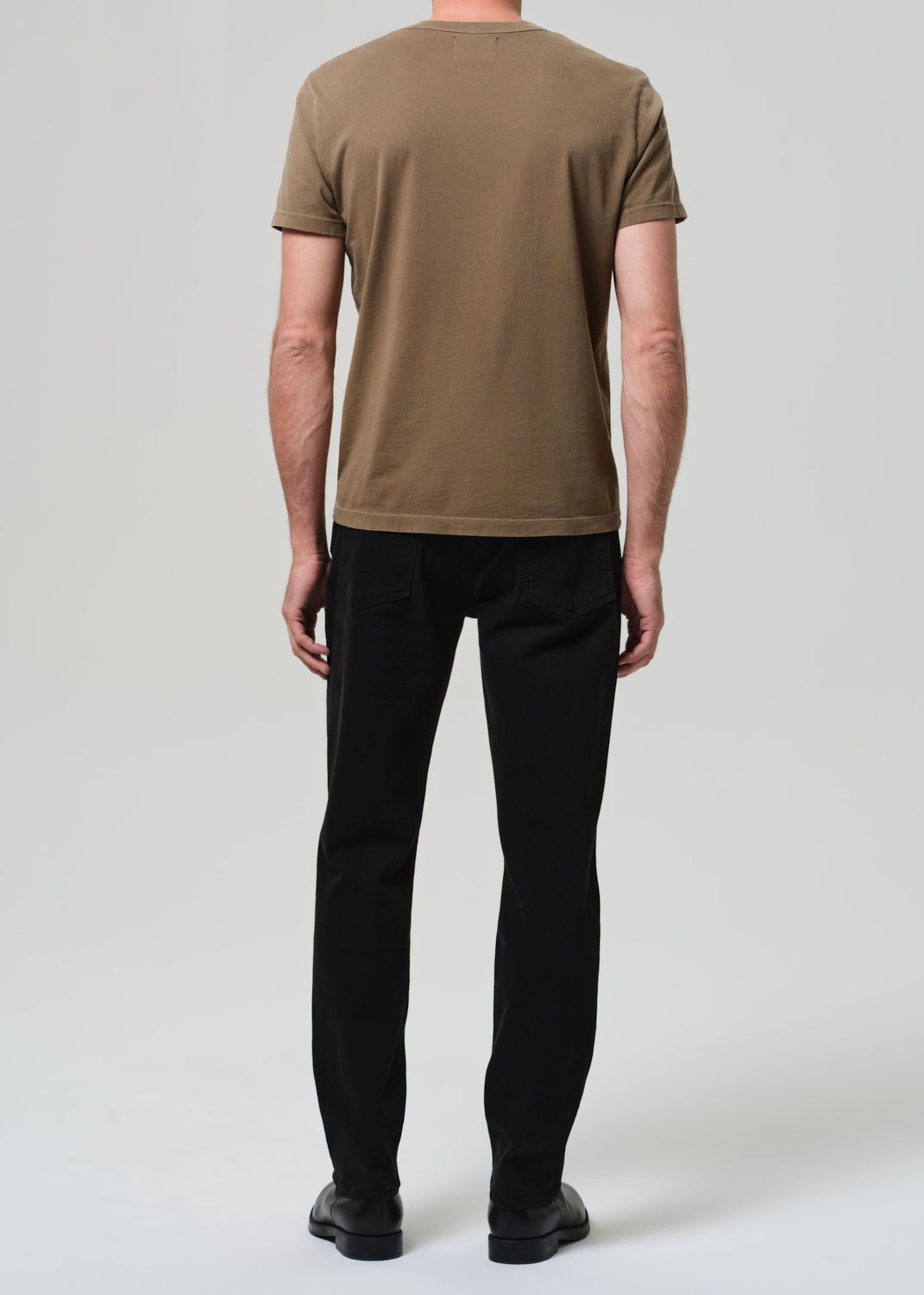 Person wearing a brown t-shirt and black pants on a white background