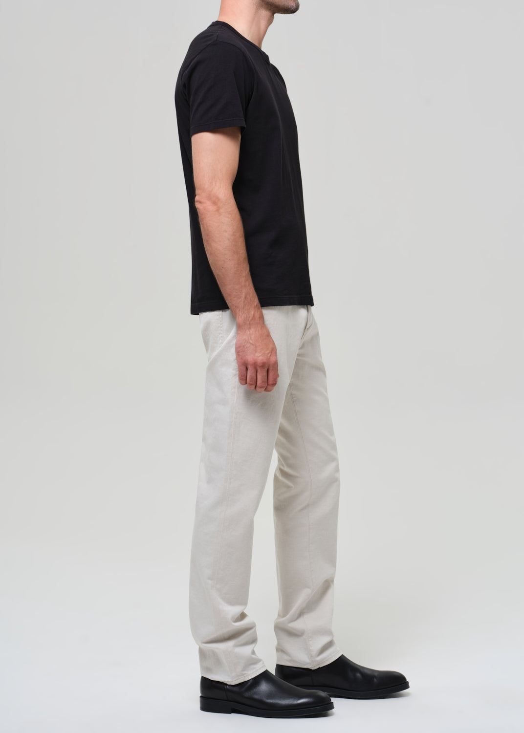 Person wearing a black t-shirt, white pants, and black shoes on a light gray background