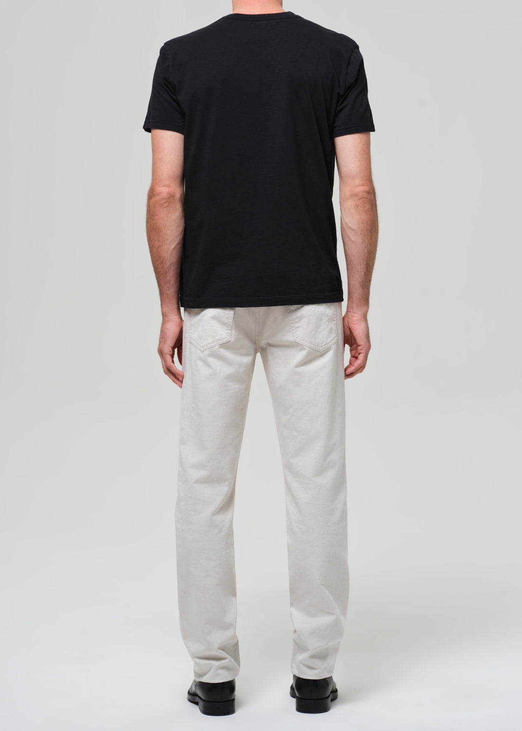 Person wearing a black t-shirt and light-colored pants on a white background