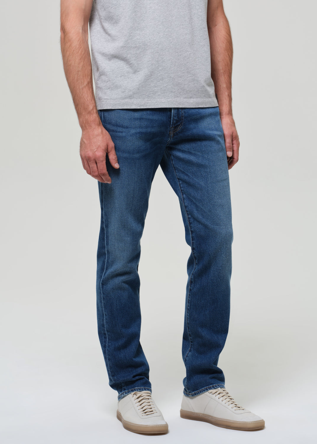 Person wearing blue jeans and a gray shirt on a plain background