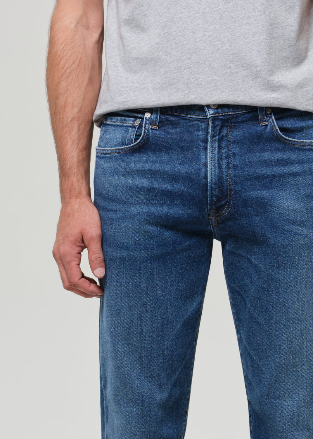 Person wearing blue jeans and a gray shirt on a plain background